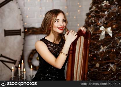 Portrait of a beautiful long-haired young girl in black Evening Dress in interior with Christmas decorations