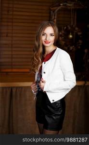 Portrait of a beautiful long-haired young girl in black leather shorts and a white jacket