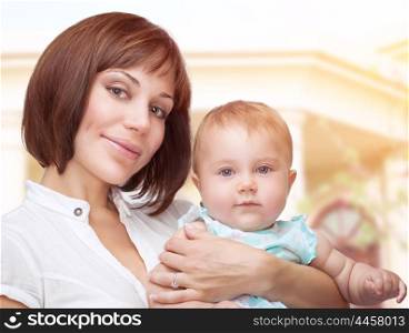 Portrait of a beautiful mother holding cute adorable baby, standing outdoor near their big new house, happy family life