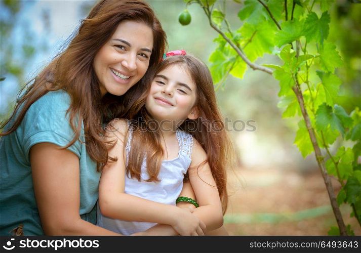 Portrait of a beautiful mother with her cute little daughter with pleasure spending time together in fresh green garden, happy family life. Happy mother and daughter portrait