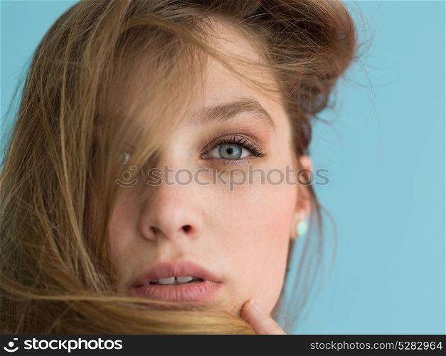 Portrait of a beautiful positive young woman while playing with her long silky hair isolated on blue background