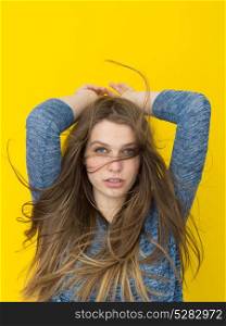 Portrait of a beautiful positive young woman while playing with her long silky hair isolated on yellow background