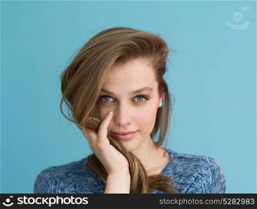 Portrait of a beautiful positive young woman while playing with her long silky hair isolated on blue background