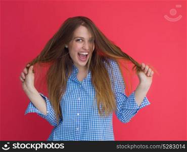 Portrait of a beautiful positive young woman while playing with her long silky hair isolated on red background