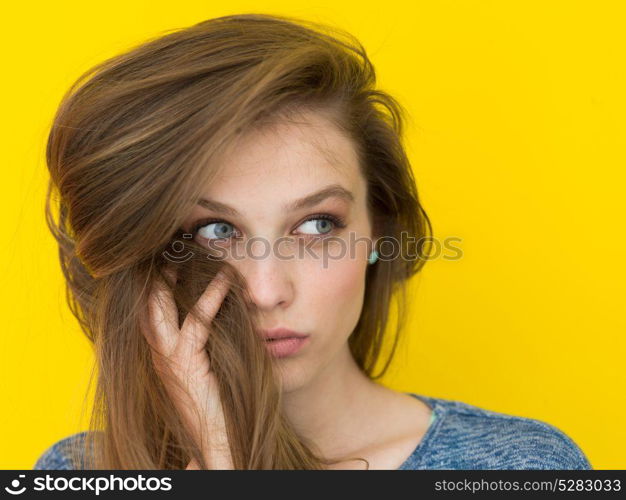 Portrait of a beautiful positive young woman while playing with her long silky hair isolated on yellow background