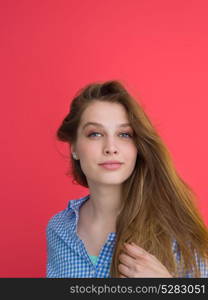 Portrait of a beautiful positive young woman while playing with her long silky hair isolated on red background