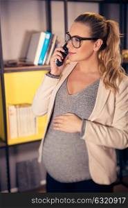 Portrait of a beautiful pregnant woman at work, expectant business woman speaking on the phone in the office, last months before maternity leave