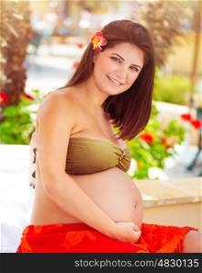 Portrait of a beautiful pregnant woman sitting on the beach, future mother spending summer holidays on a tropical resort, happy healthy pregnancy&#xA;