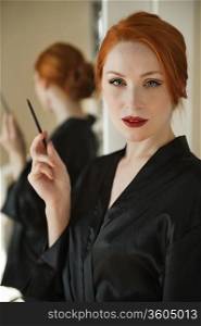 Portrait of a beautiful redheaded woman in robe holding a lip liner