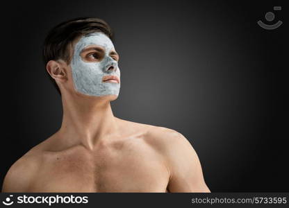 Portrait of a beautiful relaxed young man with a facial mud clay mask, face and body skin care treatment.