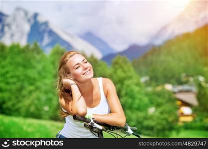 Portrait of a beautiful smiling woman enjoying bright sunny day in village in the Alps, mountainous tour on bicycle, happy active summer vacation&#xA;