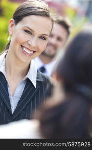 Portrait of a beautiful smiling young business woman or businesswoman with colleagues in team meeting outside