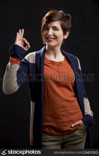 Portrait of a beautiful woman doing a OK signal, over a dark background