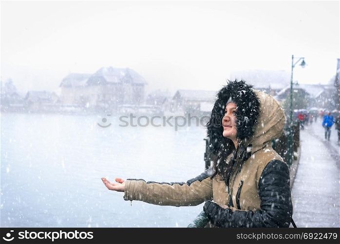 Portrait of a beautiful woman dressed for cold weather, enjoying the snowfall with her hand stretched to catch snowflakes, in the famous Hallstatt town, Austria.