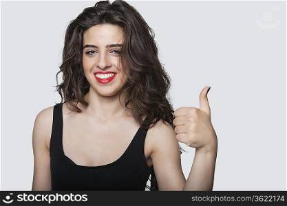Portrait of a beautiful woman gesturing thumbs up over gray background