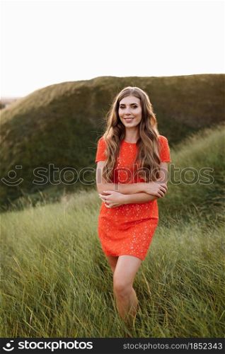 Portrait of a beautiful woman in red dress in green grass on field, nature on summer day vacation. girl with long curly hair in the park at the sunset time. Portrait of a beautiful woman in red dress in green grass on field, nature on summer day vacation. girl with long curly hair in the park at the sunset time.