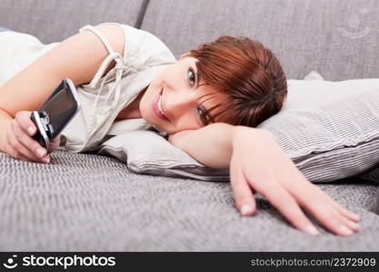 Portrait of a beautiful woman lying on sofa, sending a sms