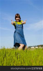 Portrait of a beautiful woman on a green meadow with thumbs up