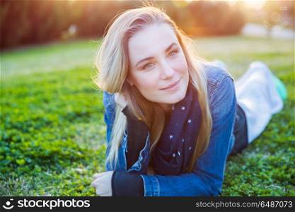 Portrait of a beautiful woman relaxing outdoors, lying down on the green grass in the park, genuine beauty of a young woman, street style look, happy healthy lifestyle. Beautiful woman relaxing outdoors