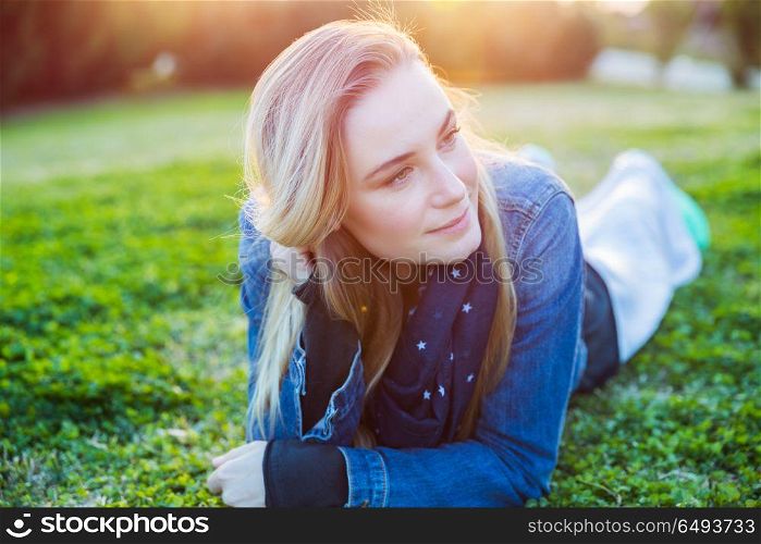 Portrait of a beautiful woman relaxing outdoors, lying down on the green grass in the park, genuine beauty of a young woman, street style look, happy healthy lifestyle. Beautiful woman relaxing outdoors