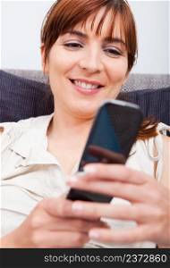 Portrait of a beautiful woman seated on sofa holding a cellphone and sending a sms