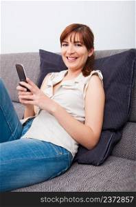 Portrait of a beautiful woman seated on sofa, sending an sms