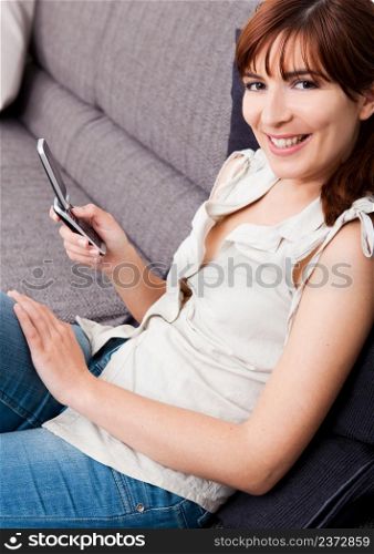 Portrait of a beautiful woman seated on sofa, sending an sms