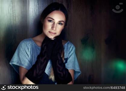 Portrait of a beautiful woman wearing natural makeup and stylish knitted gloves, stands over brown wooden background, authentic women&rsquo;s beauty. Natural women&rsquo;s beauty