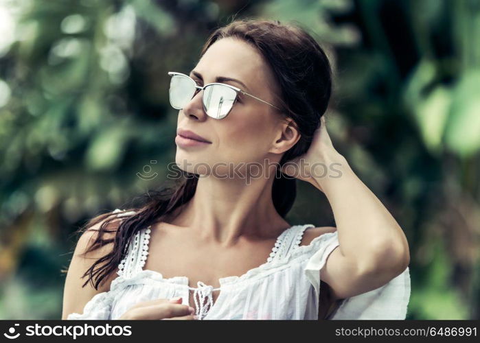 Portrait of a beautiful woman wearing stylish sunglasses over exotic plants background, luxury photoshoot on the tropical beach. Beautiful woman portrait