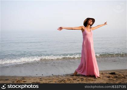 Portrait of a beautiful woman with long pink dress and sun hat on a tropical beach