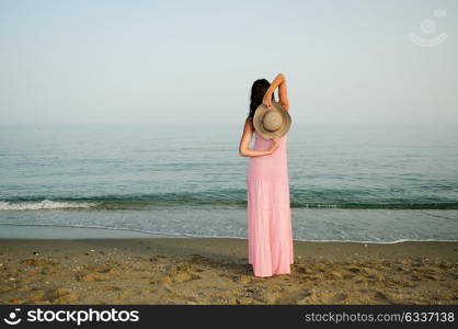 Portrait of a beautiful woman with long pink dress and sun hat on a tropical beach