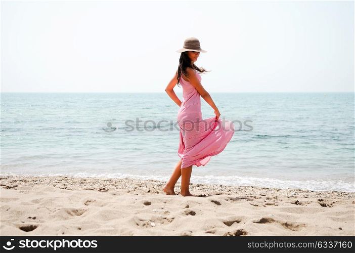Portrait of a beautiful woman with long pink dress and sun hat on a tropical beach