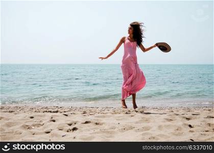 Portrait of a beautiful woman with long pink dress jumping on a tropical beach