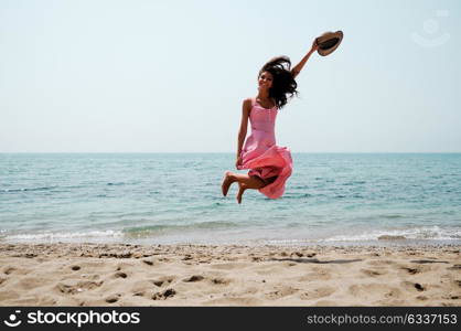 Portrait of a beautiful woman with long pink dress jumping on a tropical beach