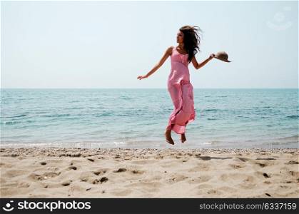 Portrait of a beautiful woman with long pink dress jumping on a tropical beach