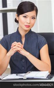 Portrait of a beautiful young Asian Chinese woman or businesswoman at a desk in her office with a pen and diary