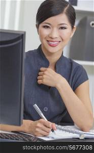 Portrait of a beautiful young Asian Chinese woman or businesswoman at the computer in her office writing in her diary