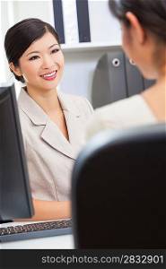 Portrait of a beautiful young Asian Chinese woman or businesswoman in office meeting with female colleague
