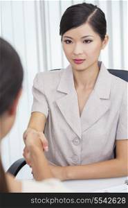 Portrait of a beautiful young Asian Chinese woman or businesswoman in office meeting with female colleague shaking hands securing a handshake deal agreement