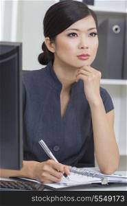 Portrait of a beautiful young Asian Chinese woman or businesswoman sitting at a desk in office writing in her personal organiser.