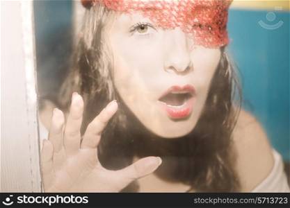 Portrait of a beautiful young brunette woman behind a dirty glass