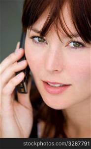 Portrait of a beautiful young brunette woman with bright green eyes talking on a mobile phone