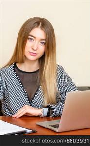 Portrait of a beautiful young caucasian woman sitting at the table working with documents looking at the camera in an office. Woman working with documents in office