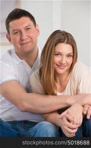 Portrait of a beautiful young happy smiling couple embracing at home while sitting on sofa