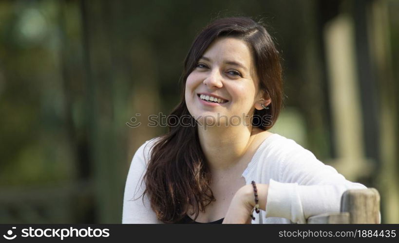 Portrait of a beautiful young Hispanic woman in the middle of a park with a very cheerful attitude against a background of unfocused green trees during sunset. Portrait of a beautiful young Hispanic woman in the middle of a park with a very cheerful attitude against a background of unfocused green trees