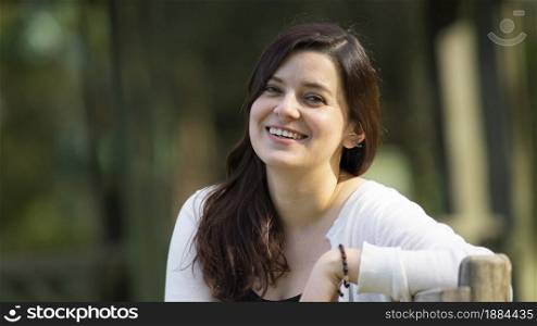 Portrait of a beautiful young Hispanic woman in the middle of a park with a very cheerful attitude against a background of unfocused green trees during sunset. Portrait of a beautiful young Hispanic woman in the middle of a park with a very cheerful attitude against a background of unfocused green trees