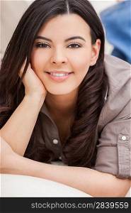Portrait of a beautiful young Latina Hispanic woman smiling laying down and relaxing at home on a sofa