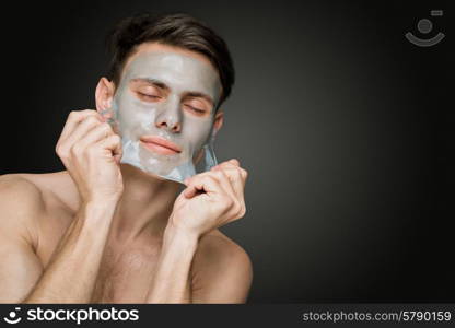 Portrait of a beautiful young man peeling off a facial mask, face and body skin care retreat.