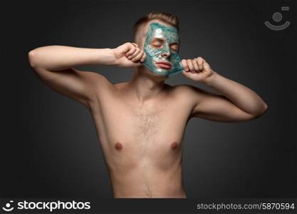 Portrait of a beautiful young man peeling off a facial mask, face and body skin care retreat.