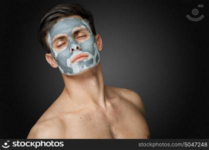 Portrait of a beautiful young man with a facial clay mask, face and body skin care treatment.